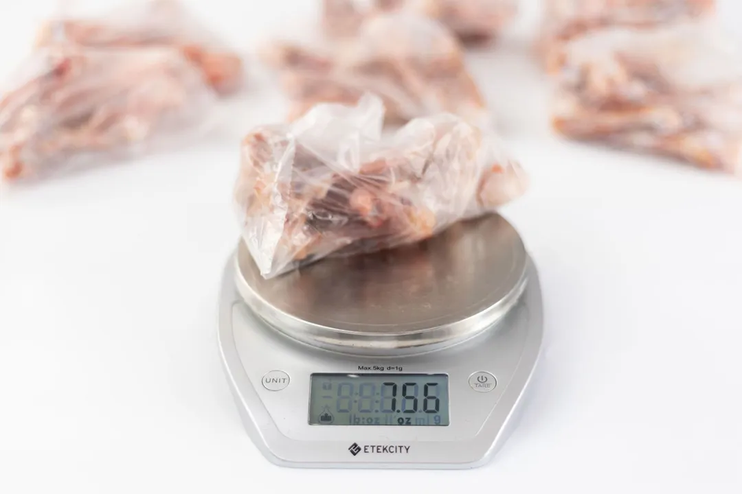 Defleshed raw chicken thigh bones in plastic bags, prepared for performance reviewing of best garbage disposals, displayed on white top. Single bag on digital scale weighing 7.56 oz.