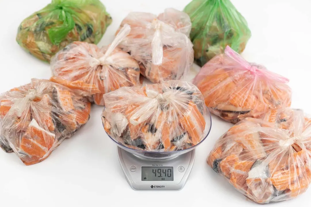 Plastic bags of raw salmon scraps displayed on white top. Bag on digital scale weighing 49.4 ounces.