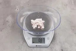 0.87 ounces of ground chicken scraps from a garbage disposal, displayed on digital scale, placed on granite-looking table. Mess of soft tissue and pieces of shredded cartilage.