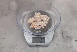 1.97 ounces of ground fish scraps from garbage disposal, displayed on digital scale, placed on granite-looking table. Mess of assorted shredded bones and raw fibrous tissue.