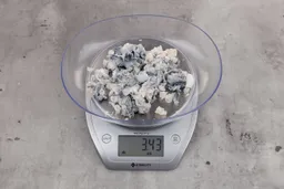 3.43 ounces of ground fish scraps from a garbage disposal, displayed on digital scale, placed on granite-looking table. Mess of shredded fish backbone and skin.
