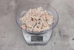 6.08 ounces of ground fish scraps from garbage disposal, displayed on digital scale, placed on granite-looking table. Pin bones among a mess of raw fibrous tissue.