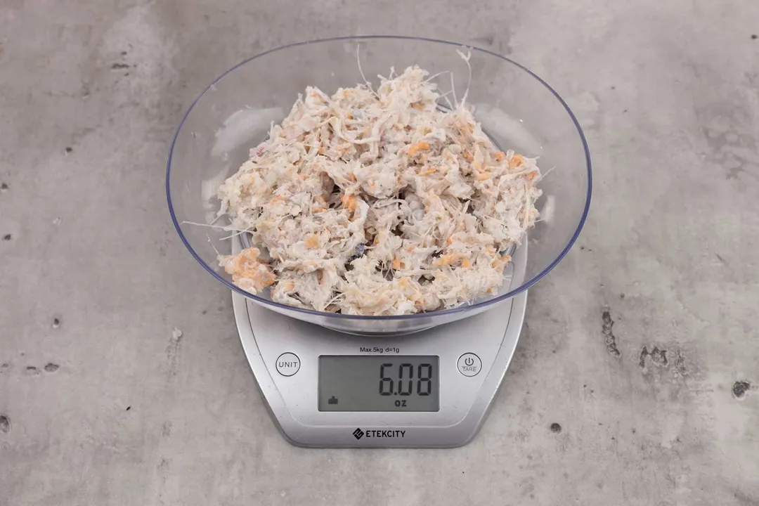 6.08 ounces of ground fish scraps from garbage disposal, displayed on digital scale, placed on granite-looking table. Visible fish pin bones among mess of uncooked fibrous tissue and assorted shredded fish bones.