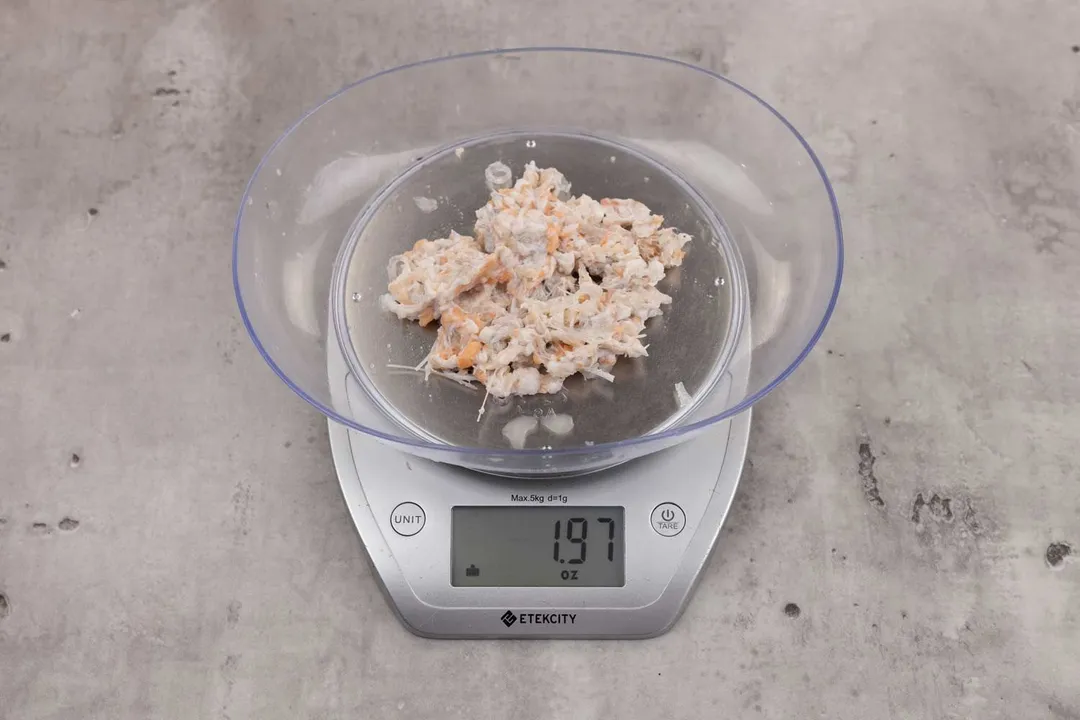1.97 ounces of ground fish scraps from garbage disposal, displayed on digital scale, placed on granite-looking table. Mess of uncooked fibrous tissue and assorted shredded fish bones