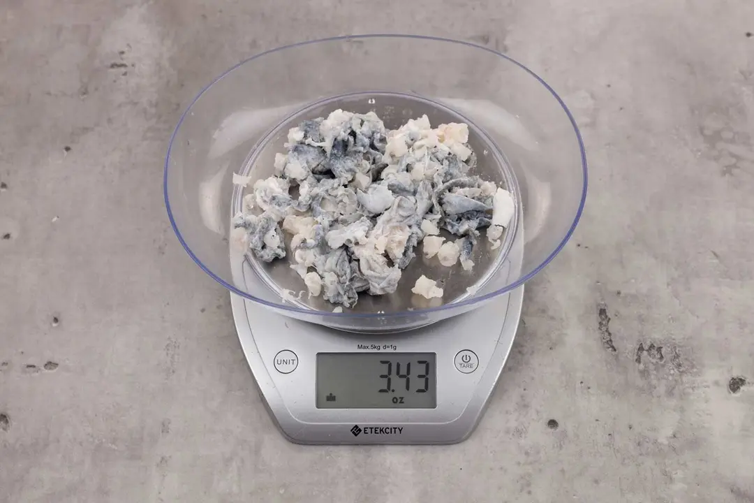 3.43 ounces of ground fish scraps from garbage disposal, displayed on digital scale, placed on granite-looking table. Mess of shredded uncooked fish skin among pieces of shredded fish backbone.