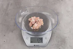 1.79 ounces of shredded soft tissue and pieces of shredded chicken bones, on digital scale, on granite-looking top.
