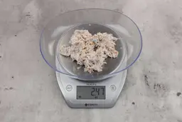 2.47 ounces of shredded bones and fibrous tissue from fish scraps, on digital scale, placed on granite-looking top.