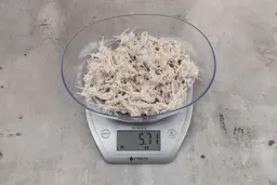 5.71 ounces of visible pin bones among mess of raw fibrous tissue from fish scraps, on digital scale, on granite-looking top.