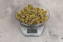 12.56 ounces of ground assorted scraps, including dietary fibers, bones, etc., on digital scale, on granite-looking top.