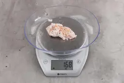 1.68 ounces of fibrous soft tissue and pieces of shredded bones, on digital scale, on granite-looking table.