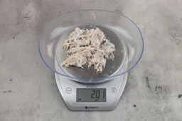 2.01 ounces of assorted fibrous tissues and shredded bones, on digital scale, on granite-looking table.