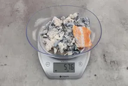 5.76 ounces of shredded fish skin among pieces of shredded backbones and one barely-shredded chop, on digital scale, on granite-looking table.