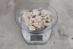 4.52 ounces of visible fish pin bones among mess of raw fibrous tissue on digital scale, on granite-looking table.