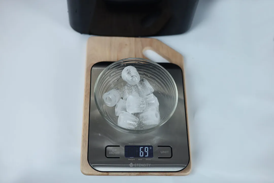 A bowl of 9 ice bullets on a scale weighing 69 grams positioned in front of a countertop ice maker.
