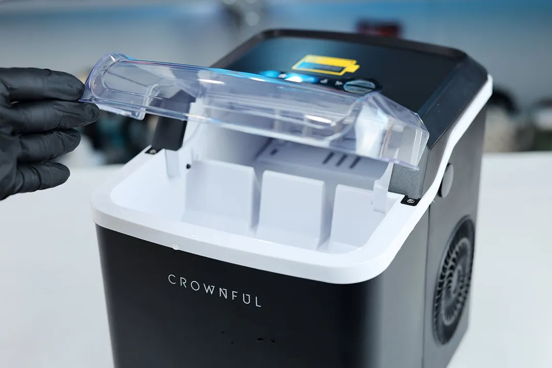 A lid to a portable ice maker being held open.