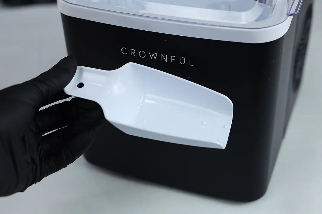 An ice scoop being held in front of a portable ice making machine.