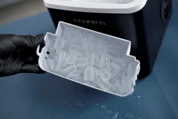 A basket full of ice being held in front of a bullet ice making machine.