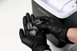 A close up of four ice bullets in a gloved hand held in front of a countertop ice making machine.
