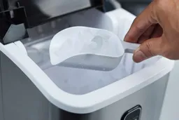 A hand scooping ice out of the ice basket of a countertop bullet ice maker.