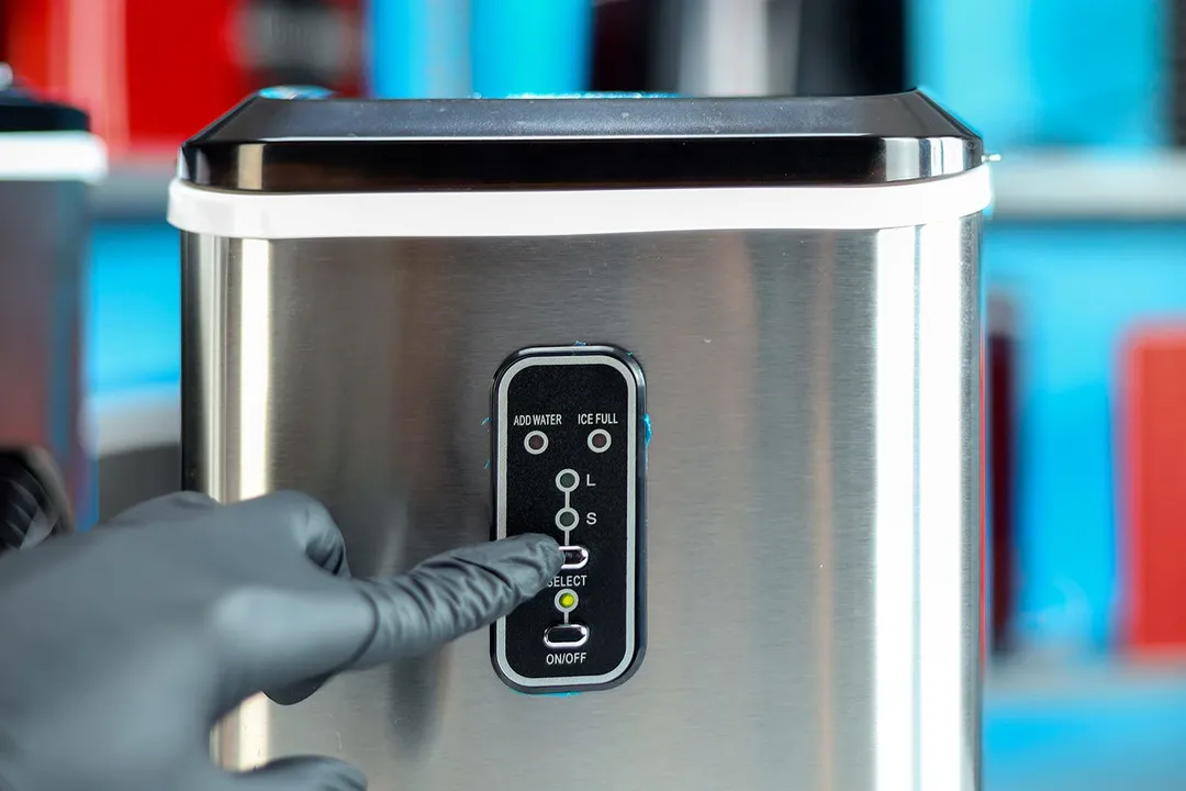 A hand pressing the select button on the EUhomy countertop ice maker with the power indicator lit up green.