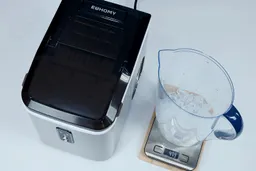 The EUhomy portable ice maker with a pitcher filled on a scale showing a net weight of ice bullets measuring grams.