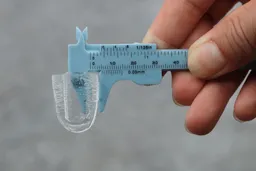 A handheld measuring device holding up an ice bullet and showing its thickness to measure 4 millimeters.
