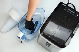 A hand reaching into a pitcher filter with a TDS meter showing zero on the reading and the Euhomy countertop ice maker to the right.