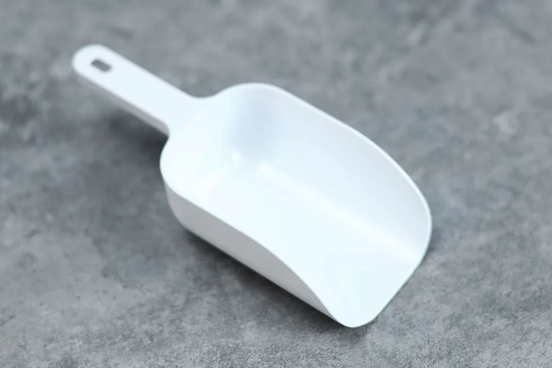 A close up of a white plastic ice scoop against a gray marble-like background.