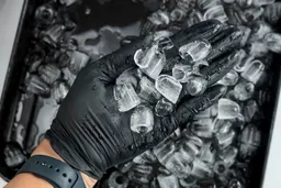 A hand with a black latex glove holding up partly melted ice from a portable bullet ice making machine.