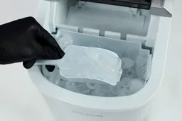 Ice being scooped out of the basket of a countertop portable ice maker.