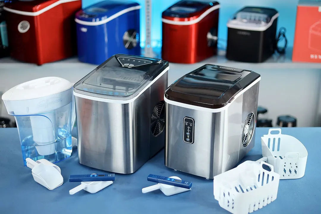Two portable bullet ice makers on a countertop with a ZeroWater pitcher to the left, a bundle of ice scoops, an ice scoop with a TDS meter in front of each machine and two empty ice baskets to the right side.