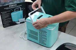 A man handling a countertop ice maker with the product box seen in the background.