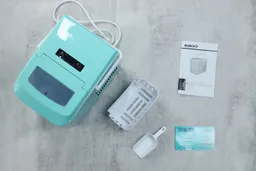 Top down view of the unpacked igloo portable ice maker. To the right of the ice maker is the removable basket, an ice scoop, the manual, and a customer service card.
