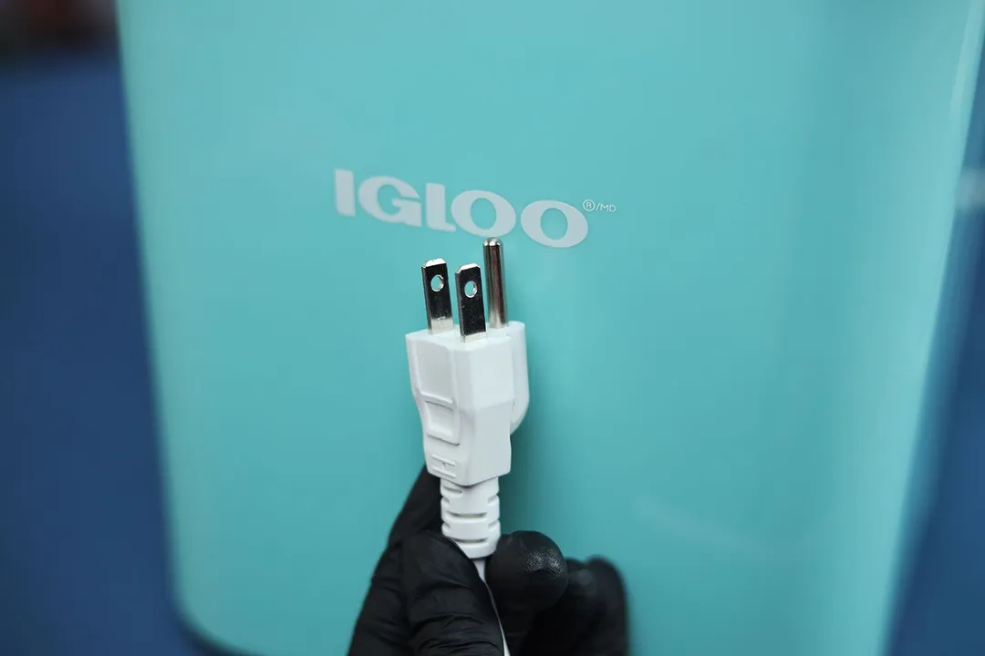 A three pronged plug being held up in front of the Igloo logo on their countertop ice making. 