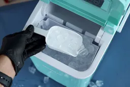 Ice being scooped up from an ice basket of a portable bullet ice maker.