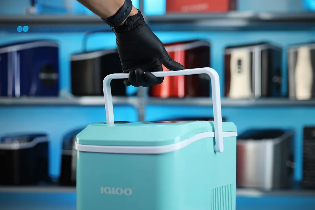 The hand gripping a countertop ice maker by lifting up the handle.