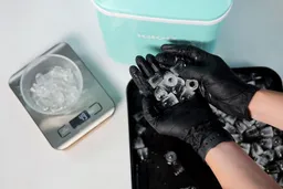 Ice being held up for close inspection with ice in a making tray in the background an a small glass bowl on a scale with broken ice weighing 49 grams
