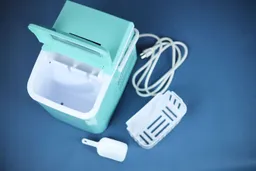 A top down view of a portable ice maker with the lid open and the removable ice basket resting at the side of the machine. 