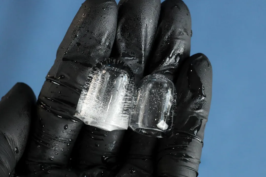 A black-gloved hand holding two typical ice bullets from a portable ice maker with a large ice bullet shown on the left, and a small bullet shown on the right.