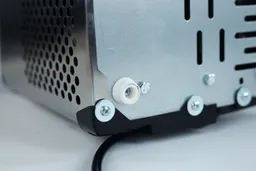 A close up of a bottom corner of a countertop ice maker showing the joinings, screws, and a leg.