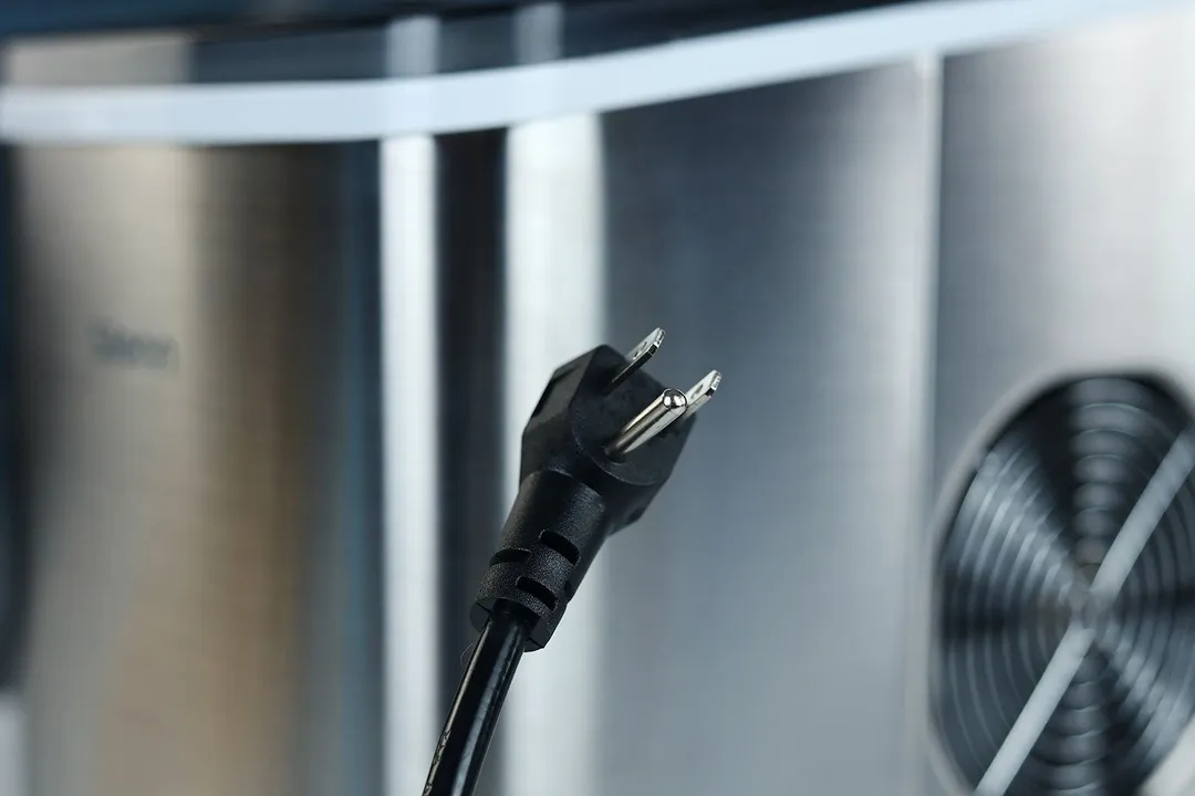 A three pronged plug at the end of a black cord picture in front of a portable ice machine which it serves