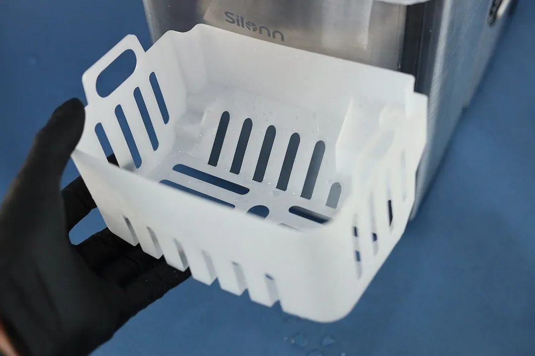 A hand holding up a plastic ice basket for a portable countertop ice maker.