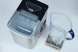 An ice machine to the left and a pitcher filled with ice bullets on a scale to the right showing production weight of 407 grams.