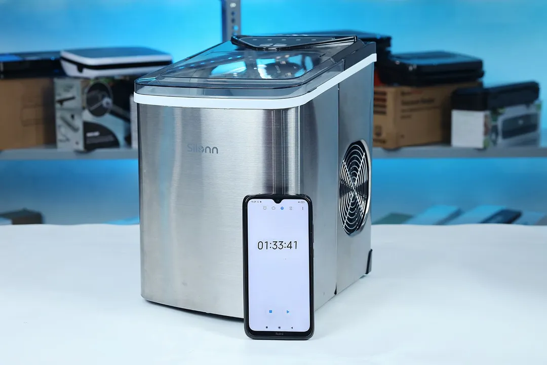 The Silonn portable ice maker on a countertop with a stopwatch resting against the front showing a full ice-making cycle taking 1 hour and 33 minutes.