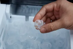 A hand holding up a chubby ice bullet produced by the Silonn countertop ice maker.