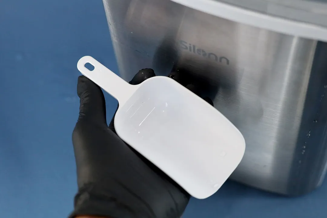 A hand holding an ice scoop in front of the Silonn countertop bullet ice maker.