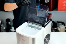 A hand touching the open lid of a portable countertop ice maker.