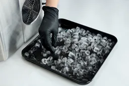 A hand examining ice in a baking tray after being left for 8-hours in a running portable countertop ice maker.