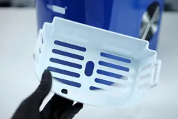 A hand holding up an empty ice basket in front of a portable ice making machine. 