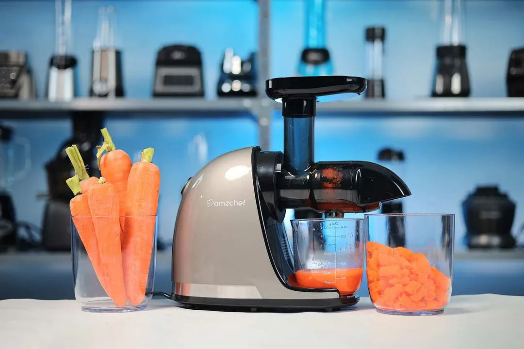 AMZChef masticator with carrot juice and pulp in its cups, next to a clear container of whole carrots